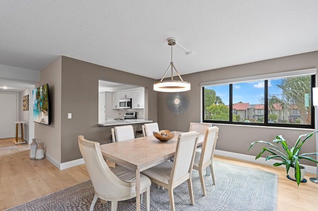 dining space featuring a textured ceiling, baseboards, and light wood-type flooring