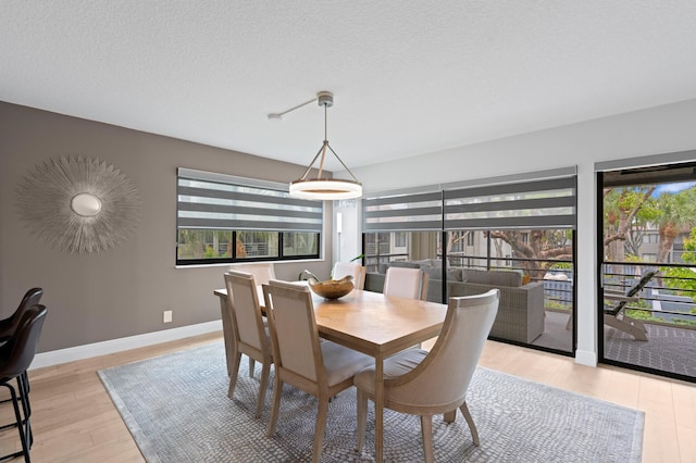 dining space with a textured ceiling, baseboards, and light wood-style flooring