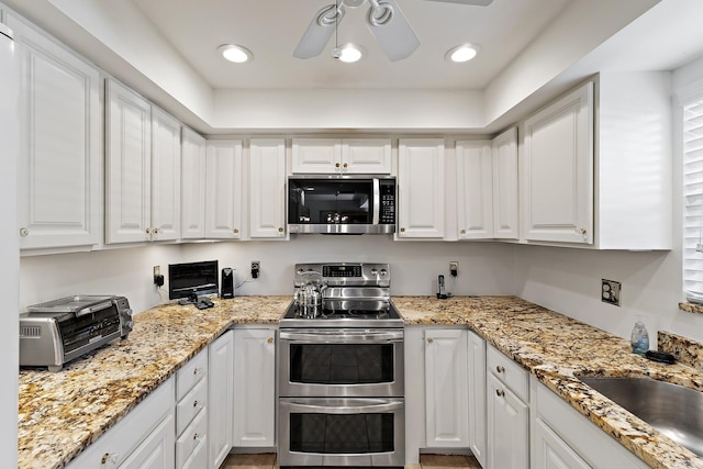 kitchen with stainless steel appliances, a ceiling fan, white cabinetry, a sink, and light stone counters