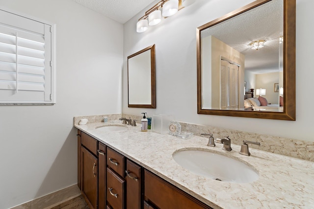 full bath with a textured ceiling, double vanity, connected bathroom, and baseboards