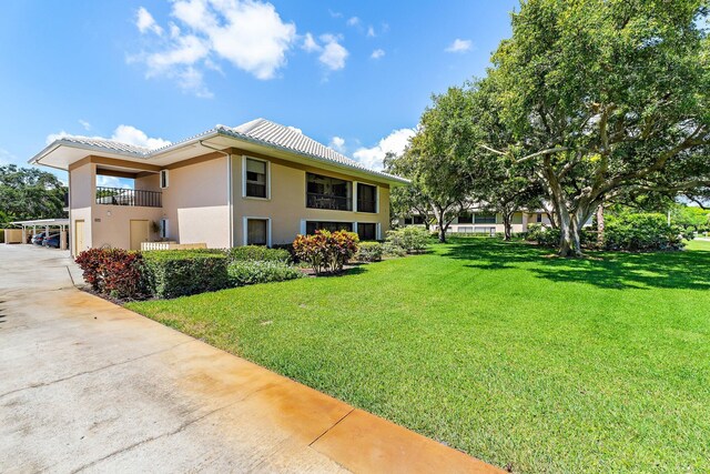 view of side of home featuring driveway, a lawn, stucco siding, a tiled roof, and a balcony