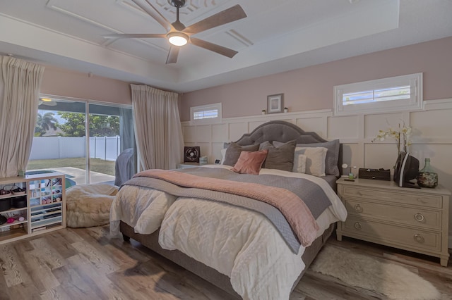 bedroom with a raised ceiling, wood finished floors, wainscoting, and access to exterior