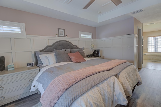 bedroom with visible vents, a decorative wall, wood finished floors, ensuite bathroom, and a wainscoted wall