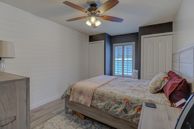 bedroom with baseboards, multiple closets, wood walls, and wood finished floors