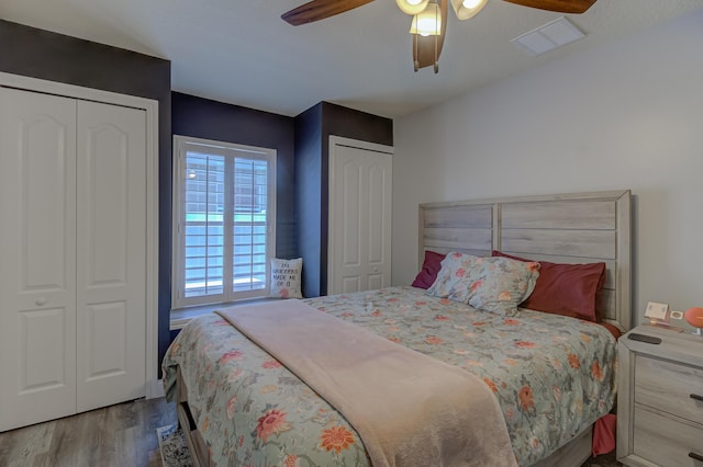 bedroom with wood finished floors, ceiling fan, two closets, and visible vents