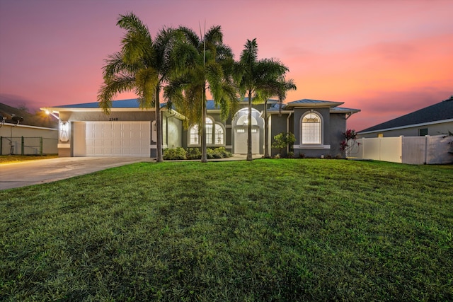 view of front of house featuring a front lawn, fence, stucco siding, an attached garage, and driveway
