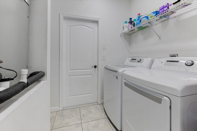 clothes washing area with light tile patterned flooring, laundry area, washing machine and dryer, and baseboards