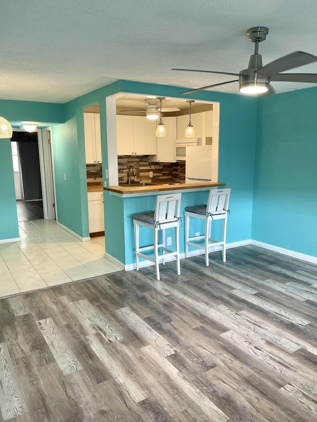 kitchen featuring decorative backsplash, a kitchen breakfast bar, wooden counters, light wood-type flooring, and white cabinetry