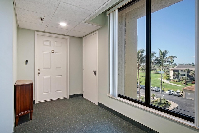 corridor with baseboards, dark speckled floor, and a drop ceiling