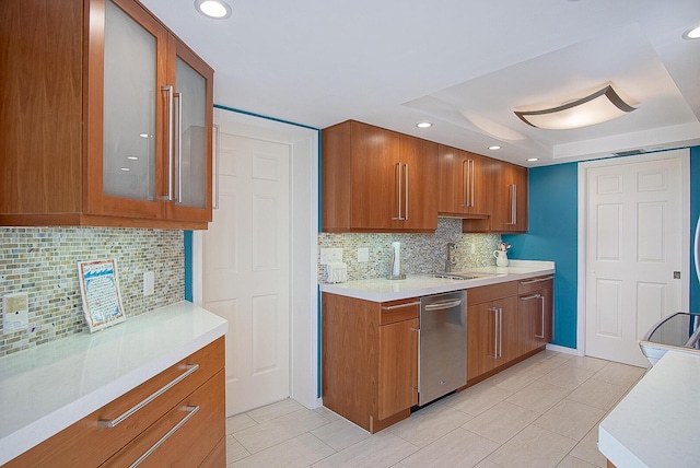 kitchen with brown cabinetry, a sink, light countertops, and stainless steel dishwasher
