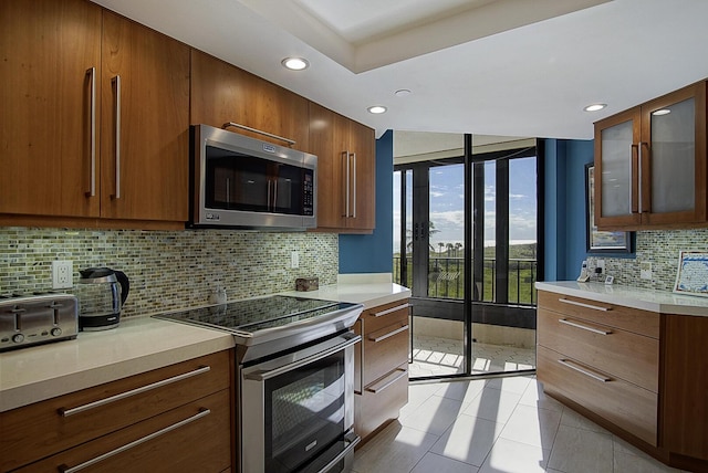 kitchen with light countertops, stainless steel appliances, decorative backsplash, and glass insert cabinets