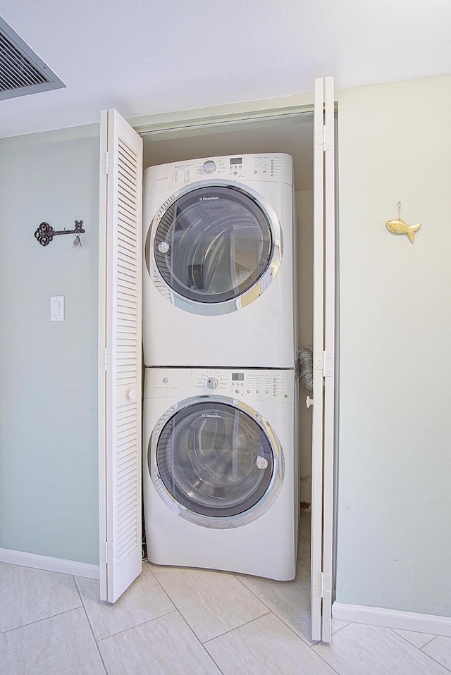 clothes washing area with tile patterned flooring, visible vents, stacked washer / drying machine, and laundry area