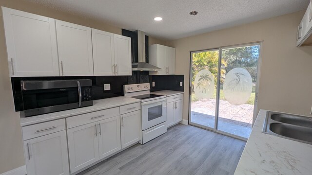 kitchen featuring wall chimney range hood, white electric stove, a sink, stainless steel microwave, and light wood-style flooring