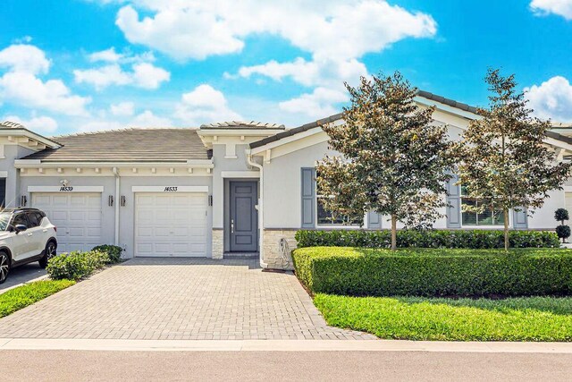 view of front facade featuring a tile roof, decorative driveway, an attached garage, stone siding, and stucco siding