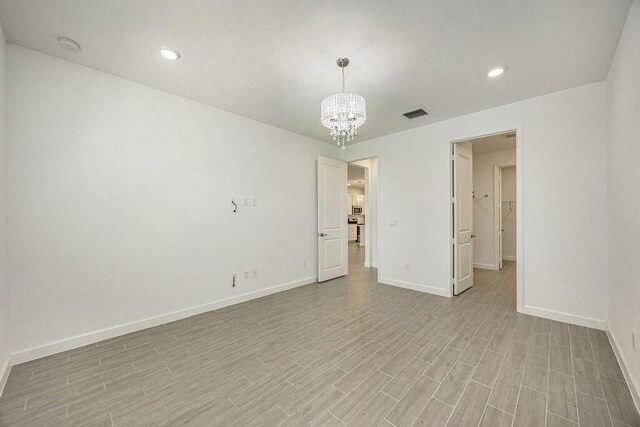 unfurnished room featuring baseboards, a chandelier, light wood-style flooring, and visible vents