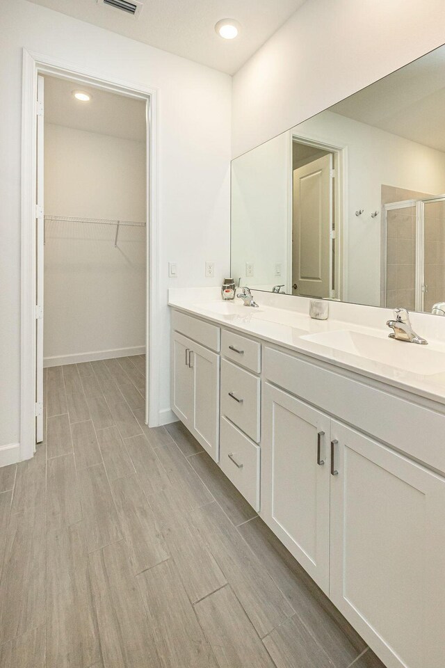bathroom with double vanity, a spacious closet, a sink, and a stall shower
