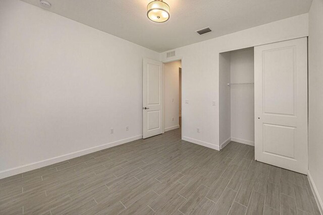 unfurnished bedroom featuring baseboards, visible vents, wood finished floors, and a closet