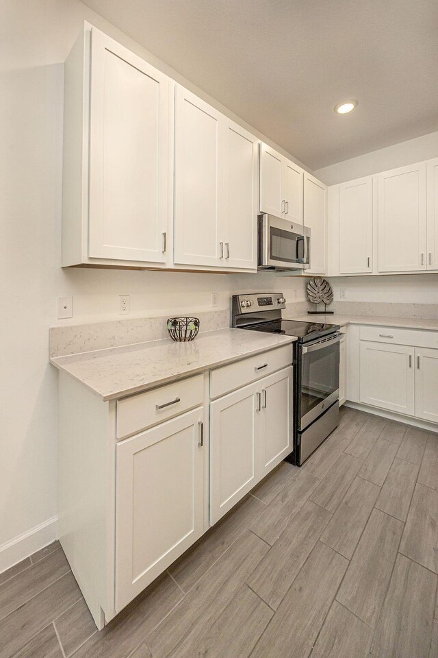 kitchen with baseboards, light wood-style floors, stainless steel appliances, recessed lighting, and white cabinetry
