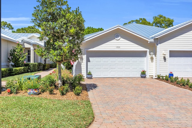 ranch-style home with an attached garage, decorative driveway, and metal roof