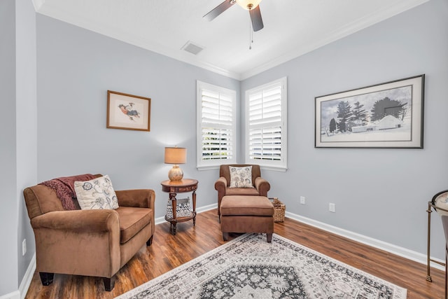 sitting room featuring a ceiling fan, visible vents, wood finished floors, baseboards, and ornamental molding