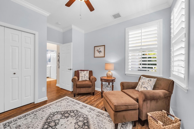 living area with a ceiling fan, baseboards, wood finished floors, visible vents, and ornamental molding