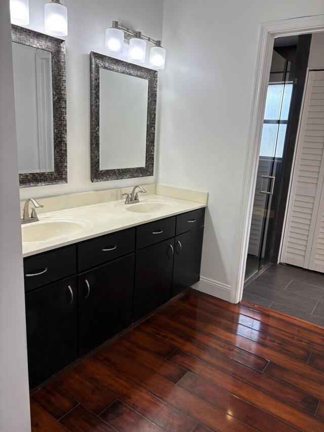 full bath with a sink, baseboards, double vanity, and wood finished floors