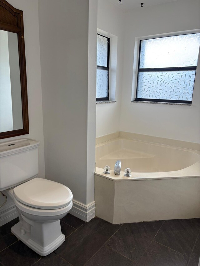 full bathroom with baseboards, tile patterned flooring, toilet, and a bath