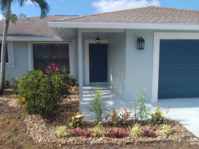 view of exterior entry featuring a garage, roof with shingles, and stucco siding