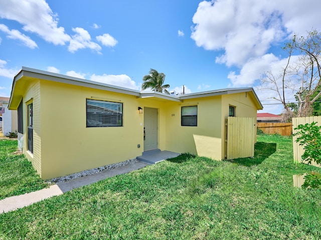 ranch-style home featuring stucco siding, a front yard, and fence