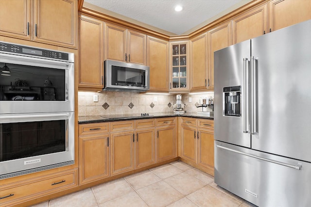 6616 NW 56th Dr, Coral Springs, FL 33067 - kitchen with appliances with stainless steel finishes, glass insert cabinets, backsplash, light tile patterned floors, and dark stone counters
