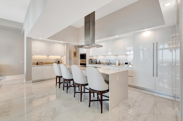 20155 Boca W Dr Unit Phc902, Boca Raton, FL 33434 - kitchen with modern cabinets, island range hood, light marble finish flooring, a kitchen bar, and white cabinetry