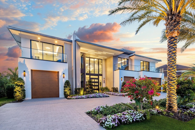 modern home featuring stucco siding, a balcony, an attached garage, and driveway