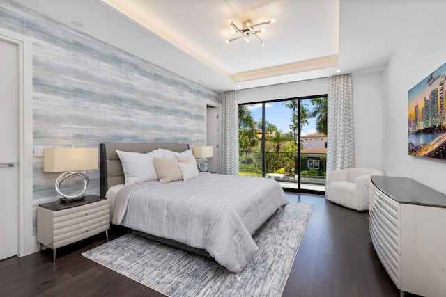 bedroom with an accent wall, dark wood-style floors, a raised ceiling, and access to outside