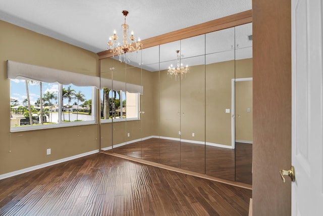 empty room featuring an inviting chandelier, baseboards, wood-type flooring, and visible vents
