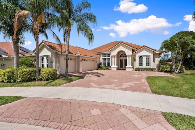 mediterranean / spanish-style home with a tiled roof, french doors, a garage, decorative driveway, and stucco siding