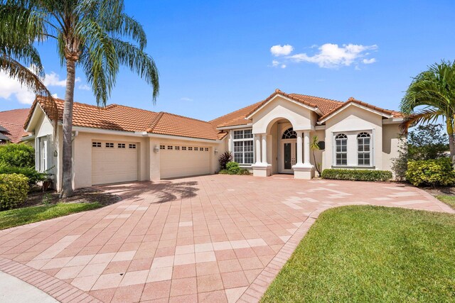 mediterranean / spanish-style house featuring a garage, stucco siding, a tile roof, and decorative driveway