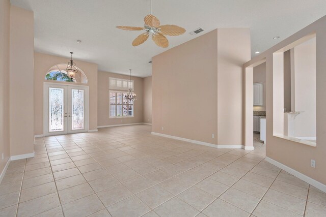 empty room featuring french doors, ceiling fan with notable chandelier, baseboards, light tile patterned floors, and visible vents