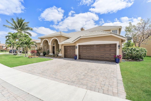 mediterranean / spanish house featuring an attached garage, stucco siding, a tile roof, a front lawn, and decorative driveway