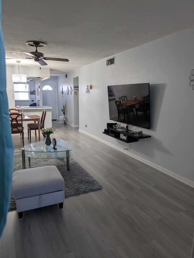 living area with baseboards, ceiling fan with notable chandelier, wood finished floors, and visible vents