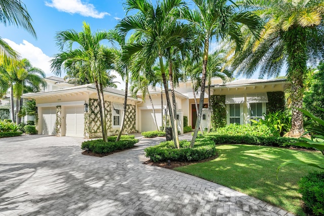 ranch-style house featuring an attached garage, decorative driveway, a front lawn, and stucco siding