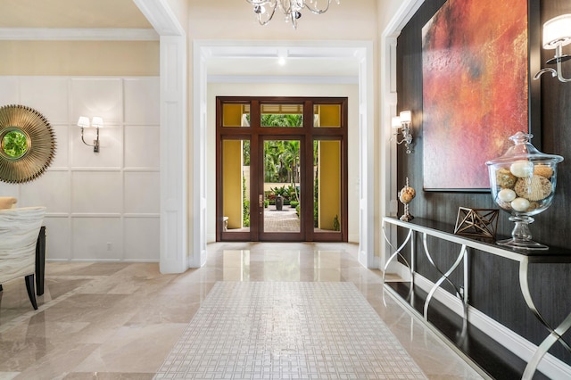 foyer with ornamental molding, marble finish floor, and a notable chandelier