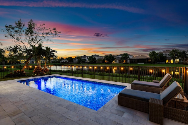 pool at dusk with a fenced backyard, a patio area, a water view, and a residential view