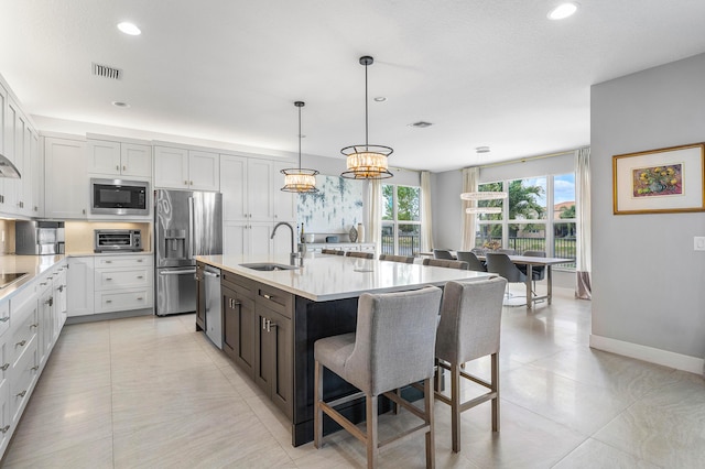 kitchen with appliances with stainless steel finishes, a sink, a breakfast bar area, light countertops, and baseboards