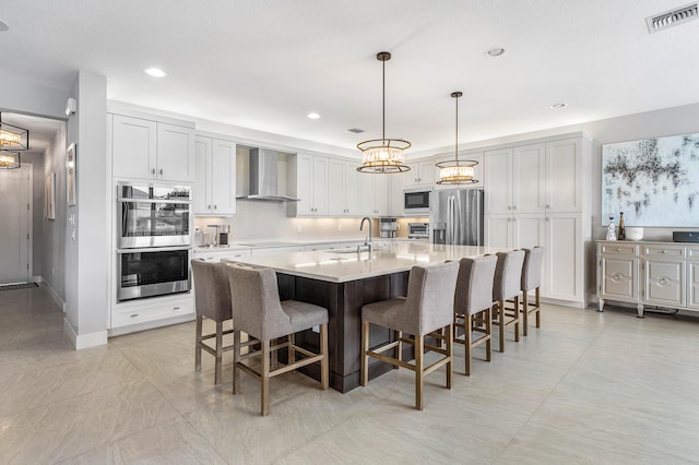 kitchen featuring wall chimney range hood, stainless steel appliances, a sink, a chandelier, and a kitchen breakfast bar