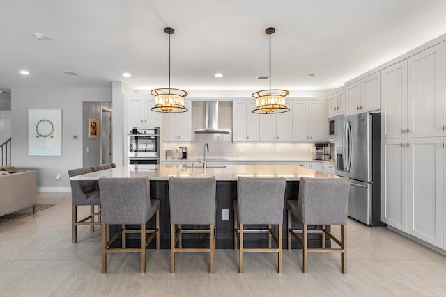 kitchen with stainless steel appliances, wall chimney range hood, light countertops, a breakfast bar area, and an island with sink