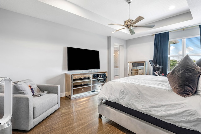 bedroom with wood finished floors, a tray ceiling, baseboards, recessed lighting, and a ceiling fan
