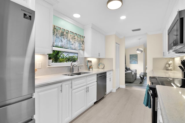 kitchen with stainless steel appliances, a sink, light countertops, white cabinetry, and ornamental molding