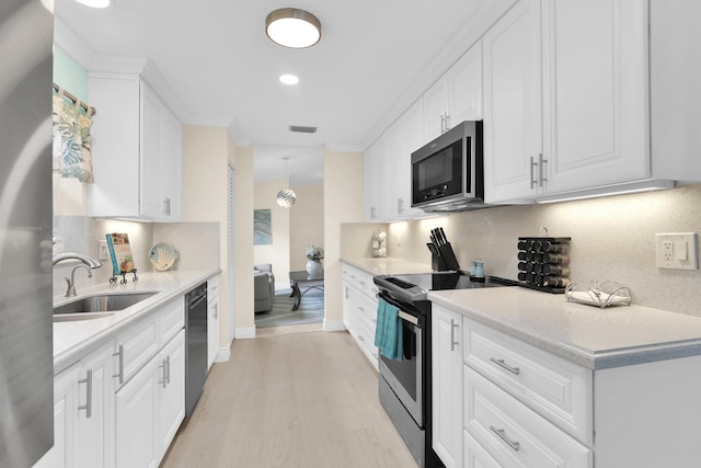 kitchen with stainless steel appliances, a sink, decorative backsplash, light wood finished floors, and white cabinets