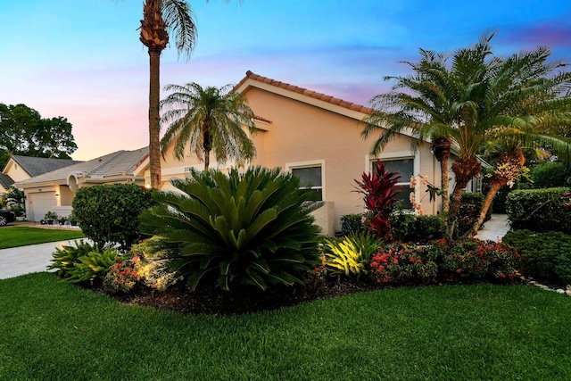 view of home's exterior featuring stucco siding, a garage, a yard, and a tiled roof