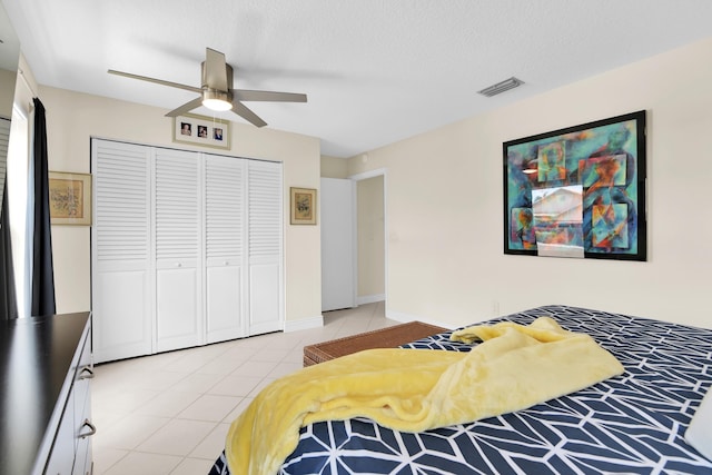 bedroom with a closet, light tile patterned floors, a ceiling fan, and a textured ceiling